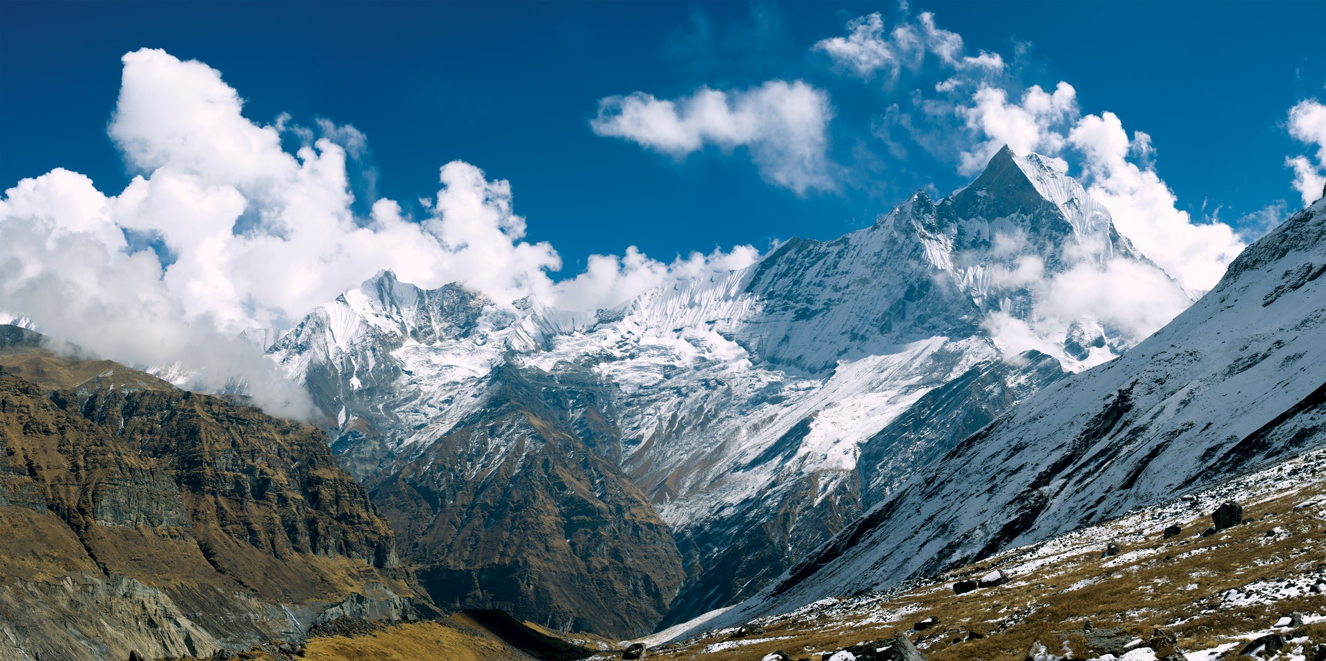 Big snowy mountains in Nepal with a light blue sky and lots of clouds